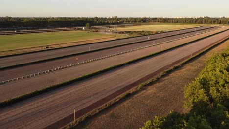 Ascending-drone-flight-above-trees-and-empty-Racecourse-of-San-Isidro-with-watering-sprinkler-after-heatwave