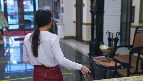beautiful woman settling into a hotel. gorgeous woman in stylish glasses doing check in and receiving the card at a reception desk. elegant lady with suitcase moving to her room in hotel.