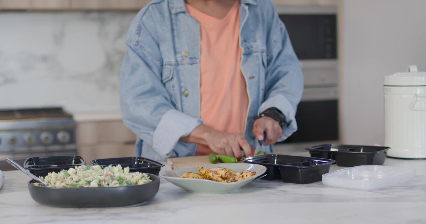 Mulher afro-americana começando a preparar refeições na cozinha, picando pimentão verde com faca e embalando caixas