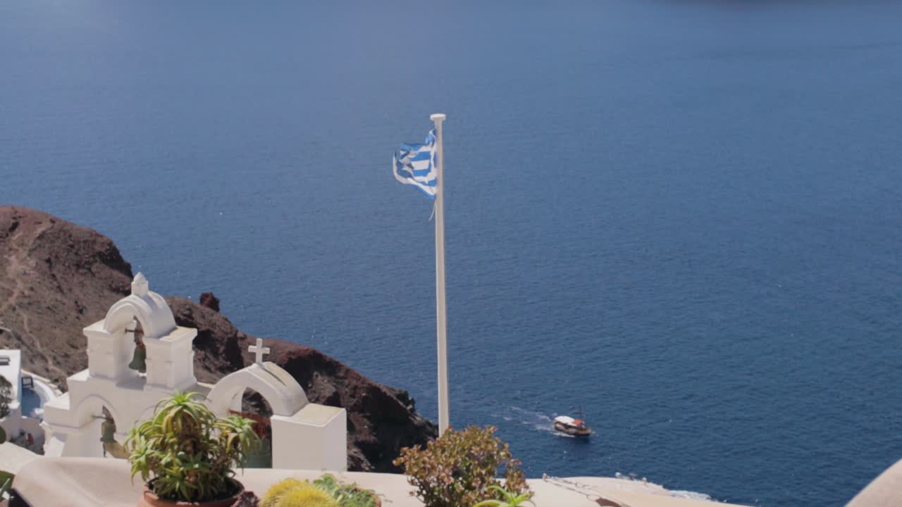 campanas de la iglesia griega y bandera con mar azul y barco en el fondo en santorini, grecia
