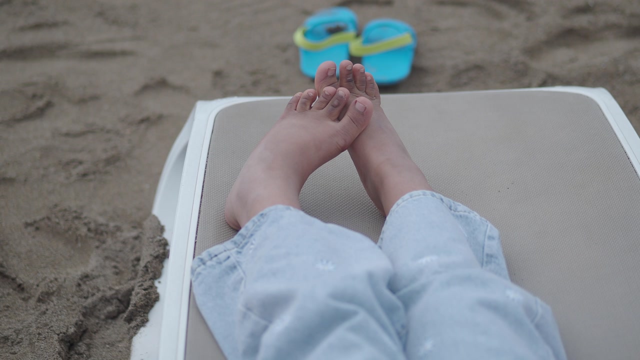 Close-up of Bare Feet Relaxing on a Sun Lounger on the Beach