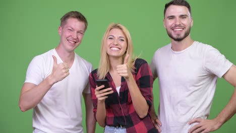 three happy young friends using phone together and getting good news