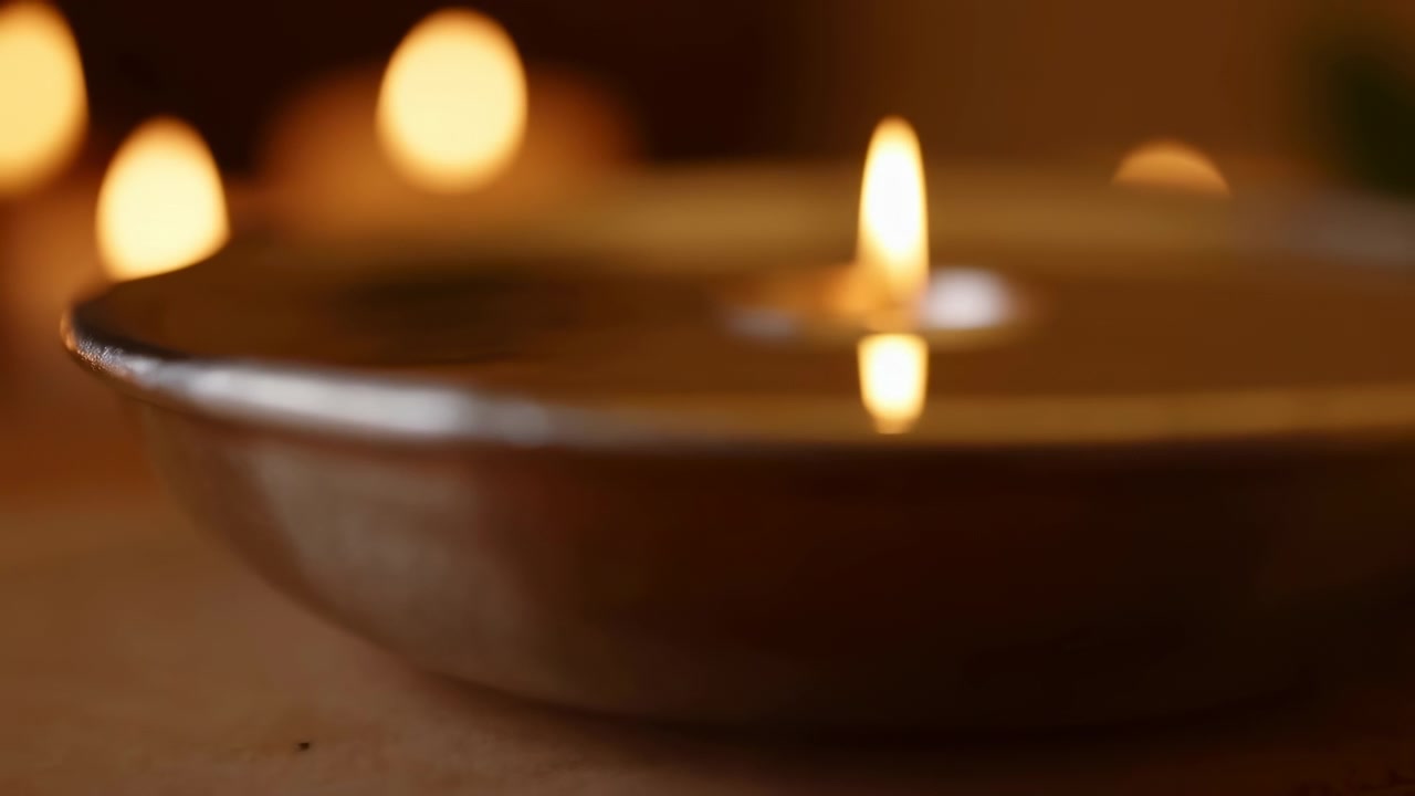 Fiamma calda e riflesso specchiato si affinano gradualmente mentre l'attenzione si sposta dal bordo testurizzato della ciotola allo stoppino centrale, con luci bokeh dorate e soffuse che brillano sullo sfondo