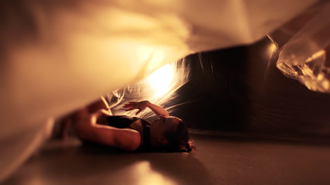 Splendido video in slow motion di un ballerino professionista che scivola sul pavimento. Si esibisce in una grotta oscura fatta di tessuto, luce e oscurità.