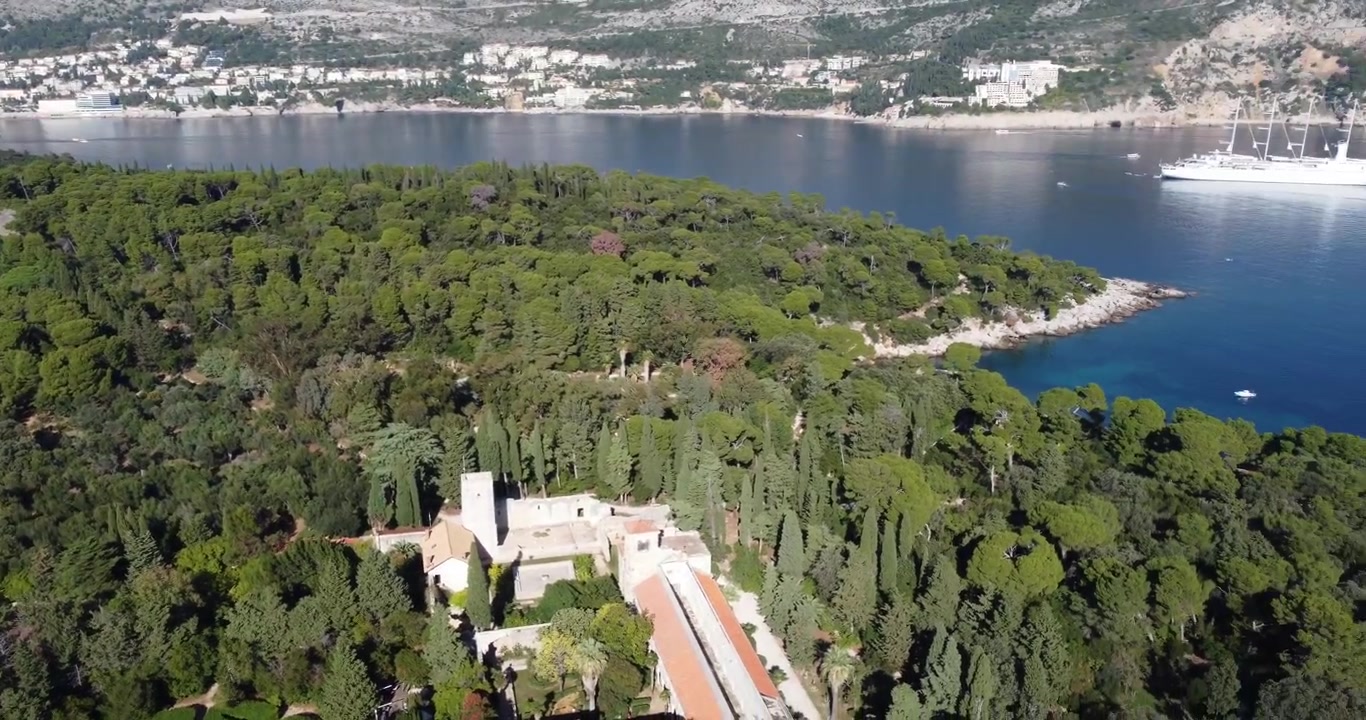 Veduta aerea dell'isola di Lokrum, che mostra il monastero e il giardino botanico, con Dubrovnik e le sue barche sullo sfondo in una soleggiata giornata estiva di tranquillità; Lokrum, Dubrovnik, Croazia