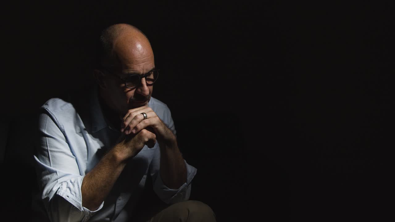 Depressed Divorced Mature Man Sitting In Darkness On Sofa Holding Wedding Ring With Low Key Lighting