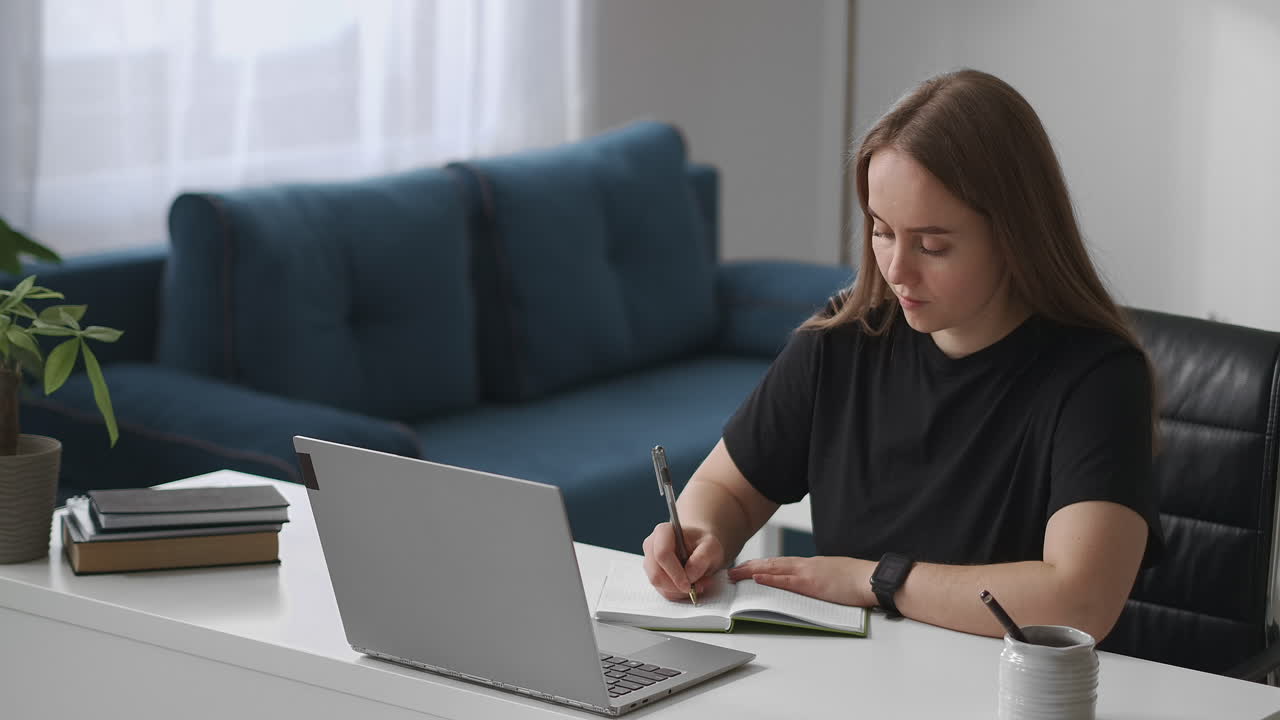 joven estudiante está escuchando una conferencia por video en una computadora portátil y escribiendo notas en un cuaderno de notas educación a distancia y aprendizaje electrónico medio retrato de mujer en la sala de estar