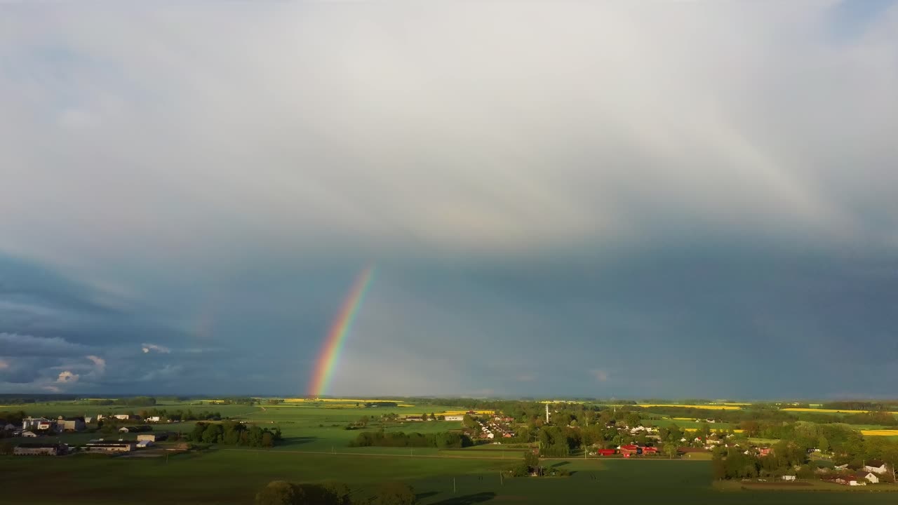 el arco iris sobre el campo de colza con canola floreciente, durante la primavera, vista aérea bajo nubes pesadas antes de la tormenta