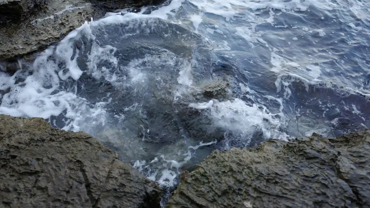 Onde che si infrangono sugli scogli vicino al centro storico di Budva, sulla costa del Montenegro, sulla costa adriatica in un soleggiato pomeriggio al tramonto. Filmato al rallentatore di onde che si infrangono in 4K