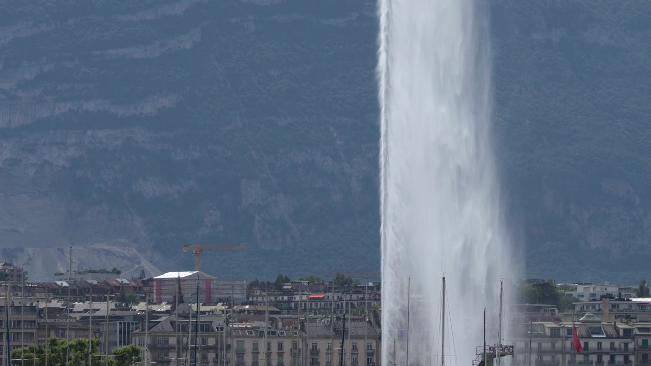Toma en contrapicado de una enorme fuente de agua contra el perfil urbano de una ciudad y montañas