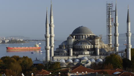 View-of-the-Blue-Mosque-in-Istanbul,-Turkey-with-big-cargo-ship-crossing-the-bosporus-strait-in-background