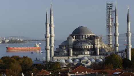 view of the blue mosque in istanbul, turkey with big cargo ship crossing the bosporus strait in background