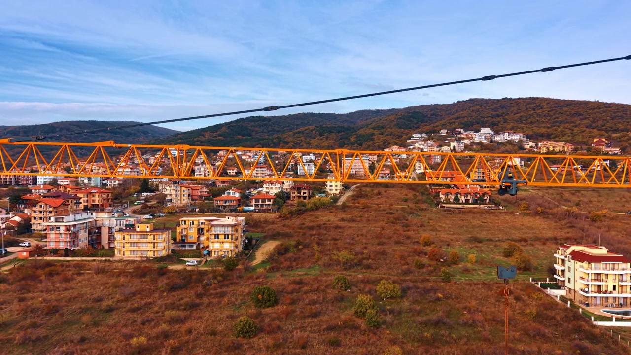 Gru a torre su un'area residenziale con una città collinare, Bulgaria. Vista a livello di drone del braccio a traliccio giallo, edifici residenziali e montagne boscose sotto un cielo nuvoloso.