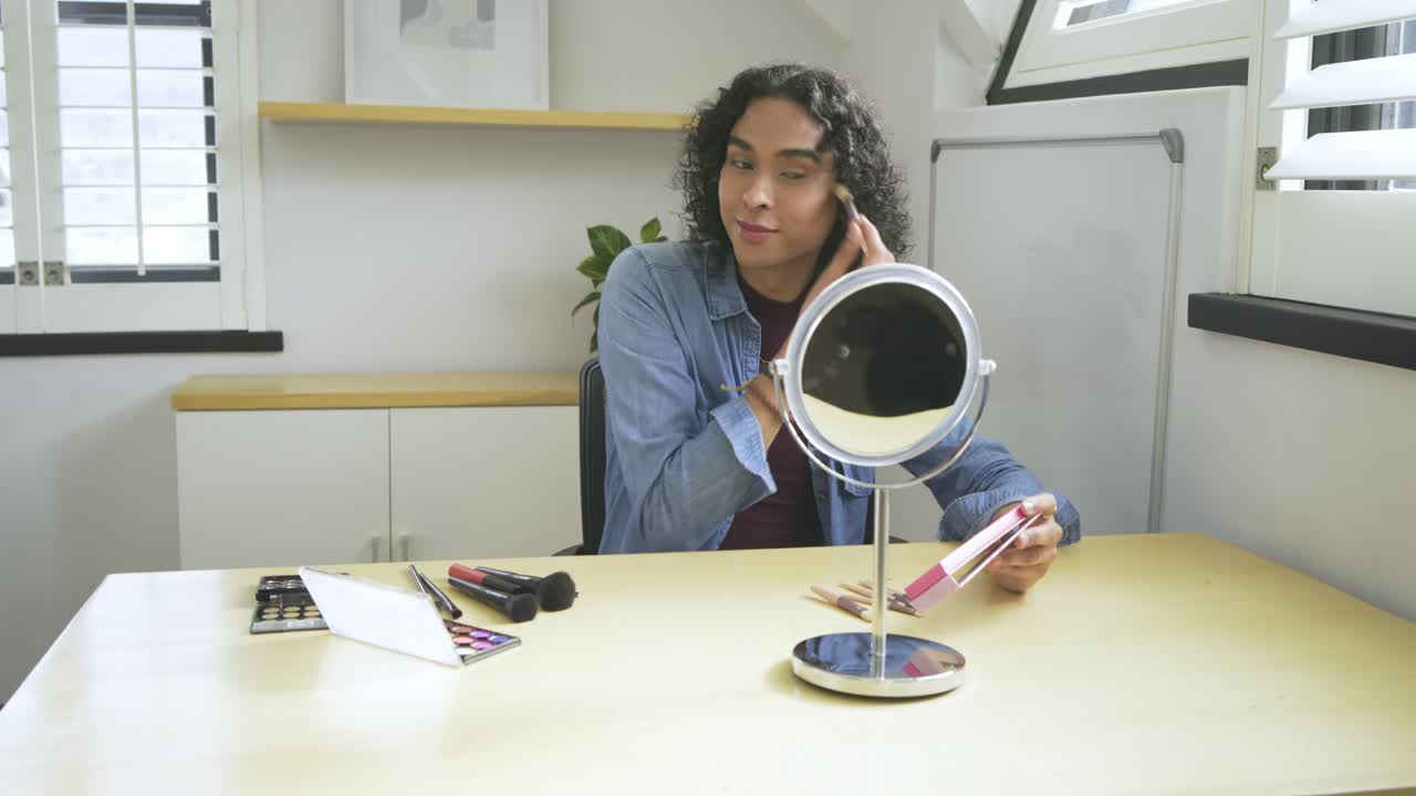 Non-binary adult using mirror, blending powder under eyes using palette and brushes at attic desk