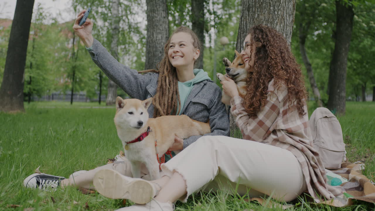 Two women taking a selfie with their dogs in a park