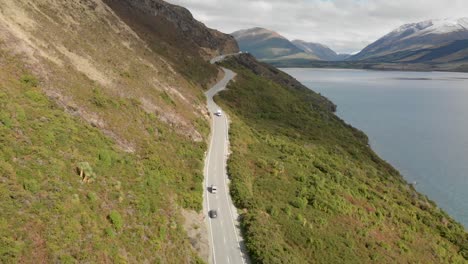 slowmo - motorhome driving in the mountains along the coast of lake wakatipu, queenstown, new zealand with mountains fresh snow in background - aerial drone