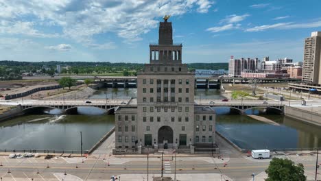 urban landscape featuring the iconic cedar rapids city hall with its distinctive golden statue, set against a backdrop of a serene river, bridges, and modern buildings under a clear blue sky