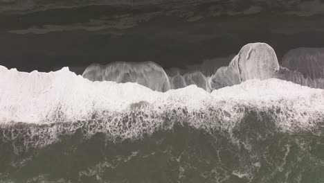 aerial shot of waves crashing against the black sand beach of reynisfjara, iceland, highlighting the powerful contrast between the white surf and dark volcanic sand.