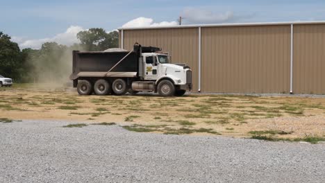 Dump-truck-full-of-white-gravel-stopping-near-a-metal-barn