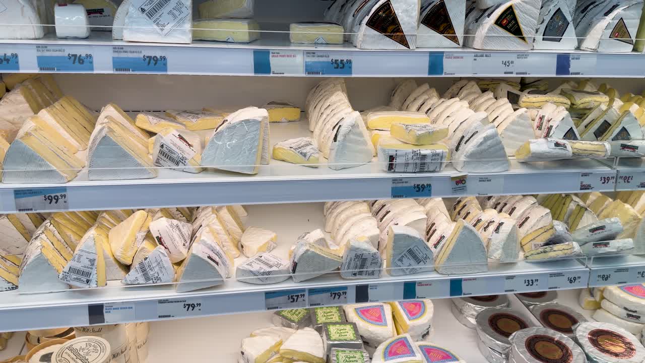 Una fluida panoramica tra gli scaffali refrigerati di un supermercato, pieni di vari formaggi gourmet