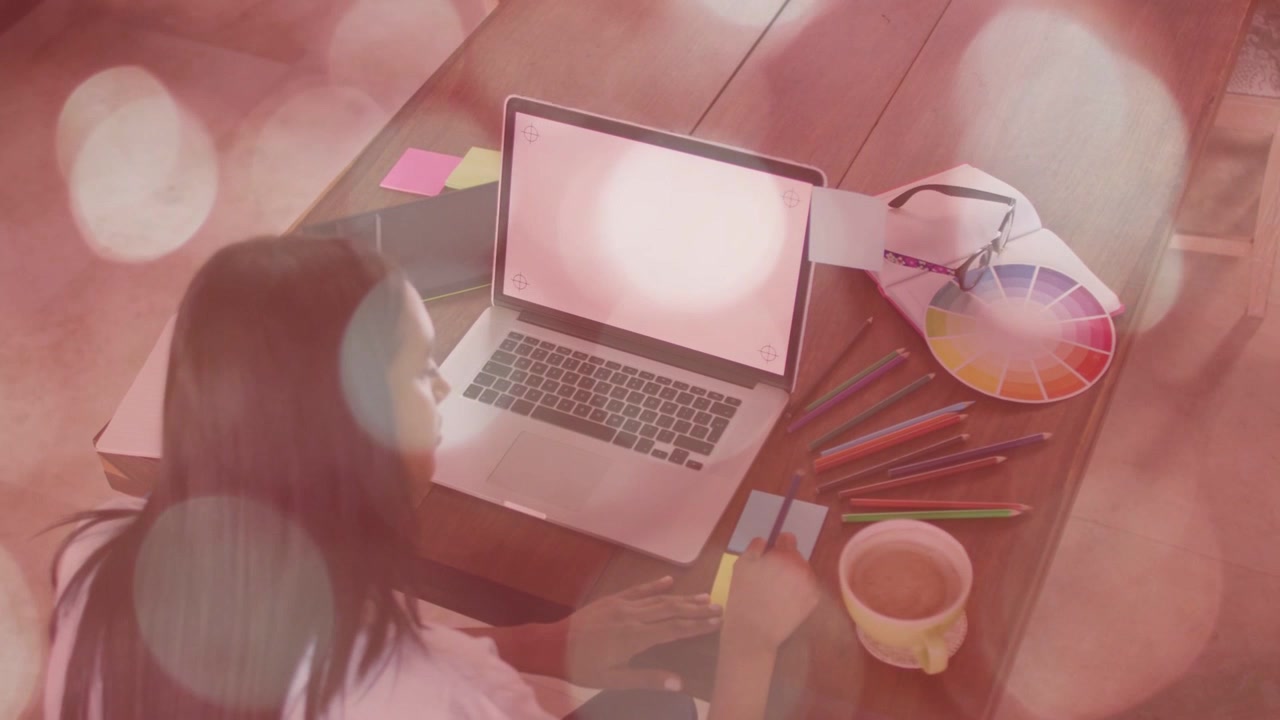 Woman designer planning, reaching yellow tab, aligning notes on laptop, bokeh overlay appearing