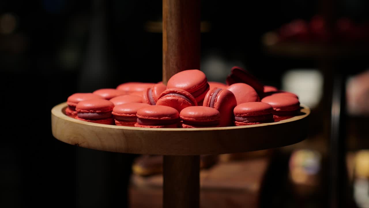 A hand picking up a red macaron from a wooden dessert stand at an elegant event.