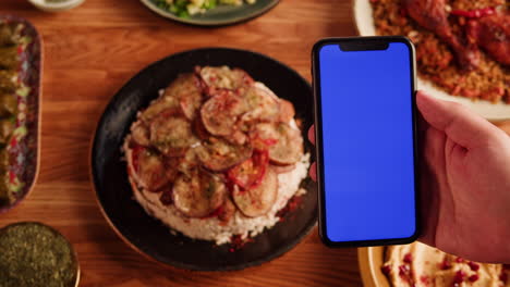 hand holding a phone displaying a blank blue screen with middle eastern food in the background