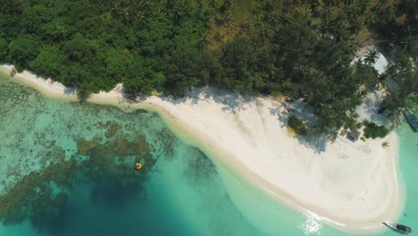 beautiful 4k uhd aerial drone shot of tropical pacific paradise beaches around islands in indonesia - thailand - asia with almost no waves, clean, clear water, a coral reef, boat, jungle forest, sand