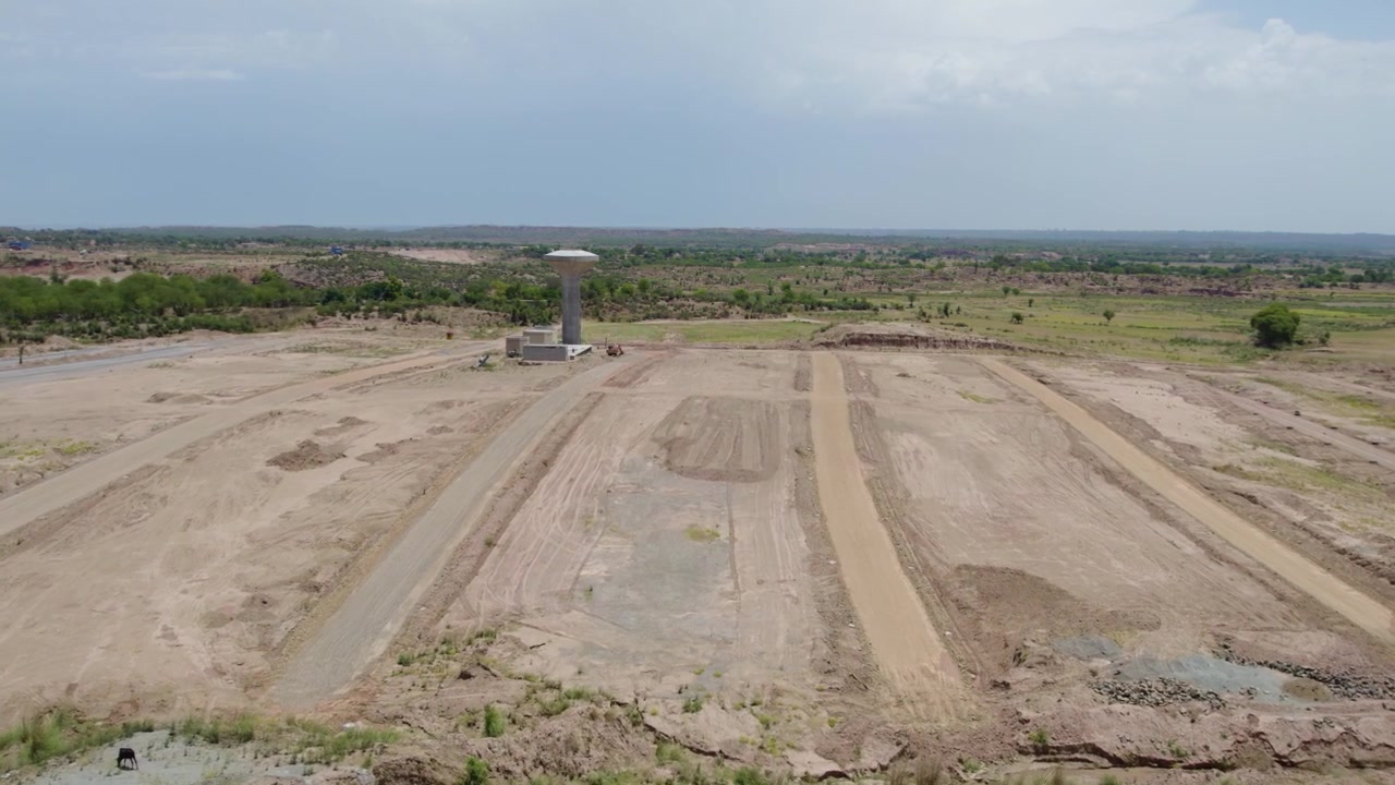 Large graded plots and dirt access routes spread across cleared land beside a distant water tower