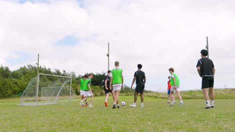 multiracial male soccer players playing soccer, running after and passing ball on pitch