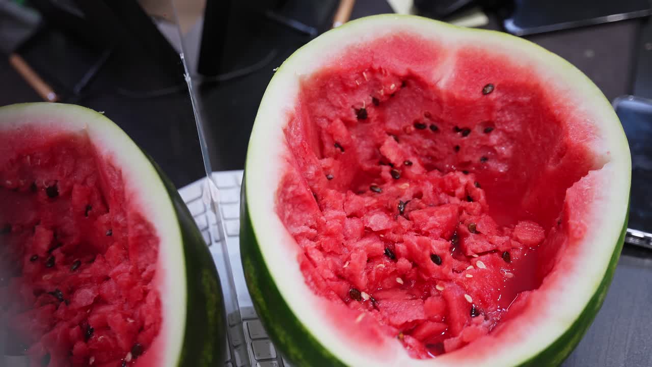 shot of a hollowed-out red watermelon resting on a white computer keyboard in a modern office. Capturing healthy snacking and summer food vibes within a workspace environment