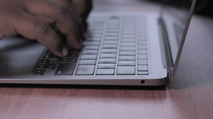 Person arbeitet an einem Laptop an einem Holzschreibtisch.