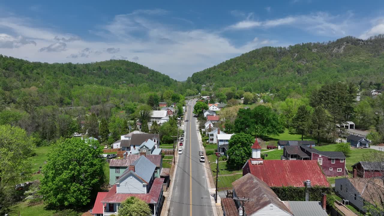 Straight street with parking cars in small american town during sunny day. Blue sky and green mountains at hillside of Virginia. Aerial tilt up wide shot.