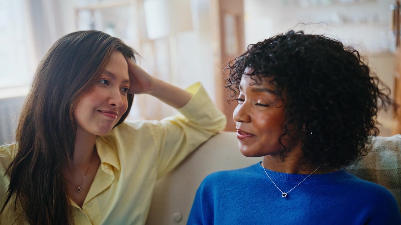 Girlfriends sharing heartfelt talk home sofa. Emotional support close friends.