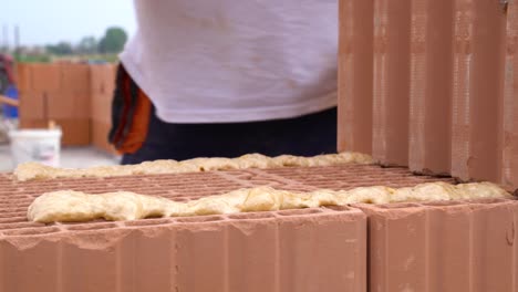ceramic brick lowered onto adhesive foam layer during house wall construction