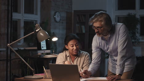 two diverse coworkers collaborating at a desk in an office at night