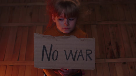 afraid homeless toddler girl sitting holding inscription no war, hiding from bombing attack at home