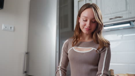 una giovane donna felice danza gioiosamente mentre si occupa di attività in cucina, la cucina moderna presenta armadietti eleganti, frigorifero in acciaio inossidabile e presa a parete sullo sfondo