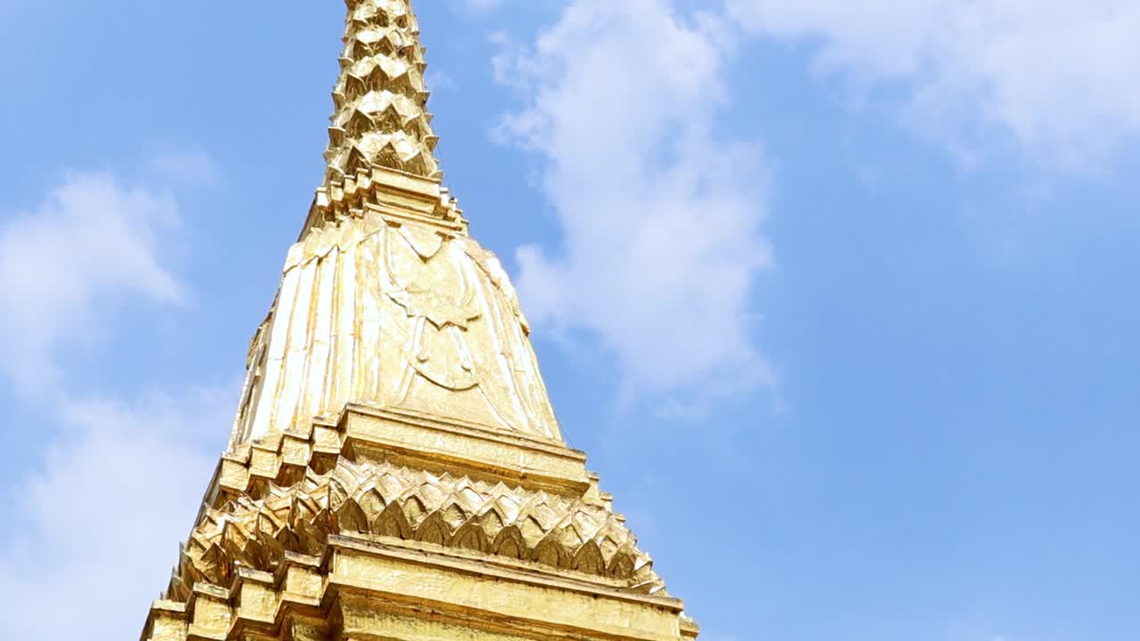 Close-up view of a golden spire with intricate details set against a bright blue sky.