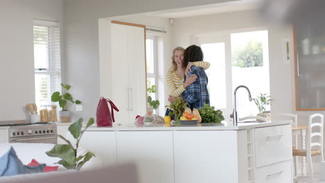 happy diverse couple embracing and unpacking shopping bags in ktichen, slow motion