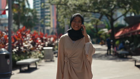 young muslim woman talking on phone while walking in urban park