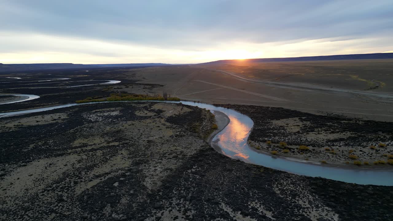 Aerial view of a blue Patagonian river winding through the Pampa at sunset, glowing in soft golden light