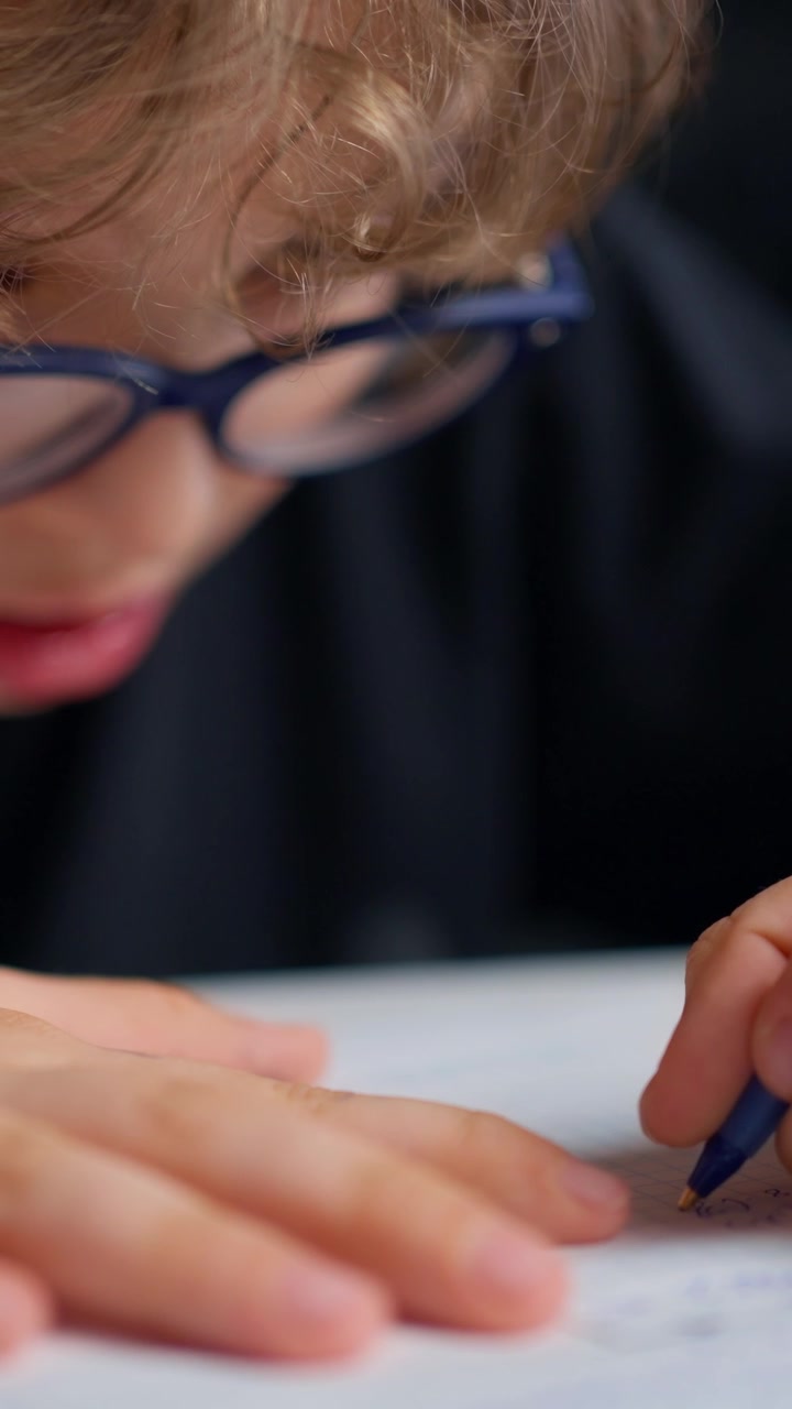 Primo piano di un bambino con gli occhiali che scrive su carta