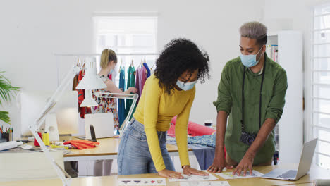 female fashion designer and male photographer wearing face mask discussing with each other in studio