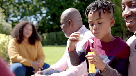 Felices-Padres-Afroamericanos-Con-Abuelo-E-Hijo-Soplando-Burbujas-En-Un-Jardín-Soleado