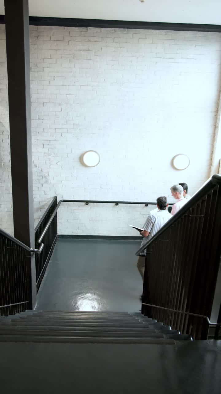 Vídeo vertical: Equipo diverso subiendo las escaleras y hablando sobre un portátil porque tienen que entregar un trabajo