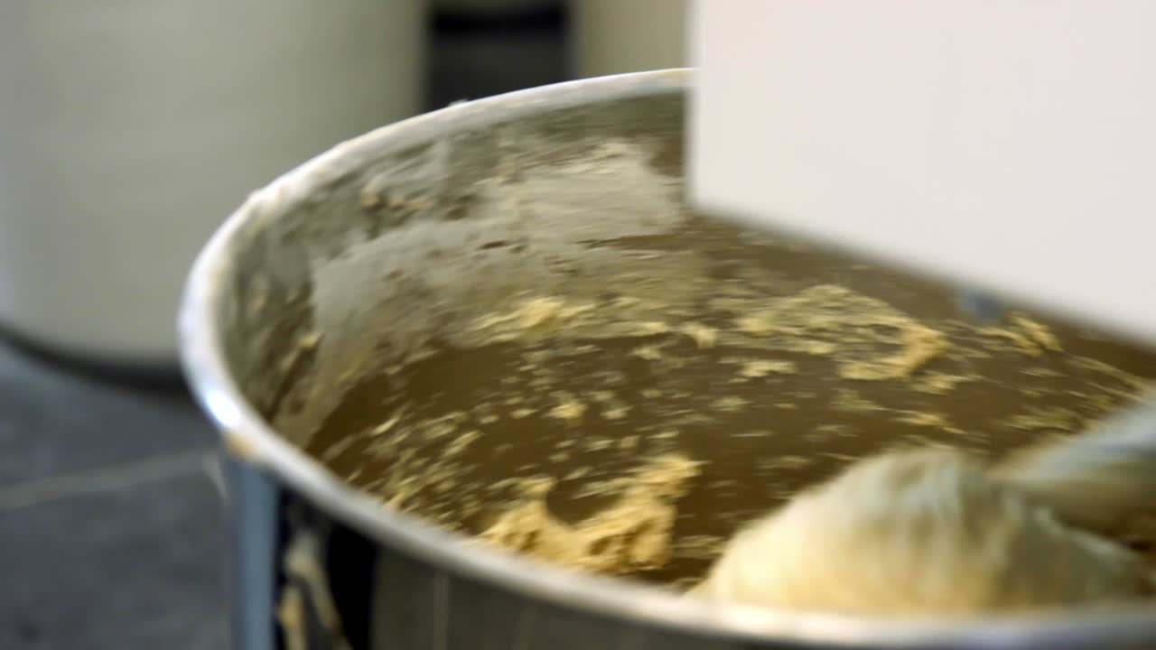 Fornaio che tocca l'impasto in un'impastatrice industriale, primo piano.
