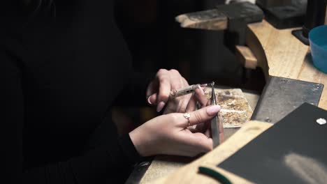 shot of a female metalworker using a syringe and some tweezers to make adjustments to a silver metal necklace