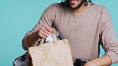 Mensajero-Sacando-Comida-De-La-Mochila,-Aislado-Sobre-Fondo-Azul-Del-Estudio.