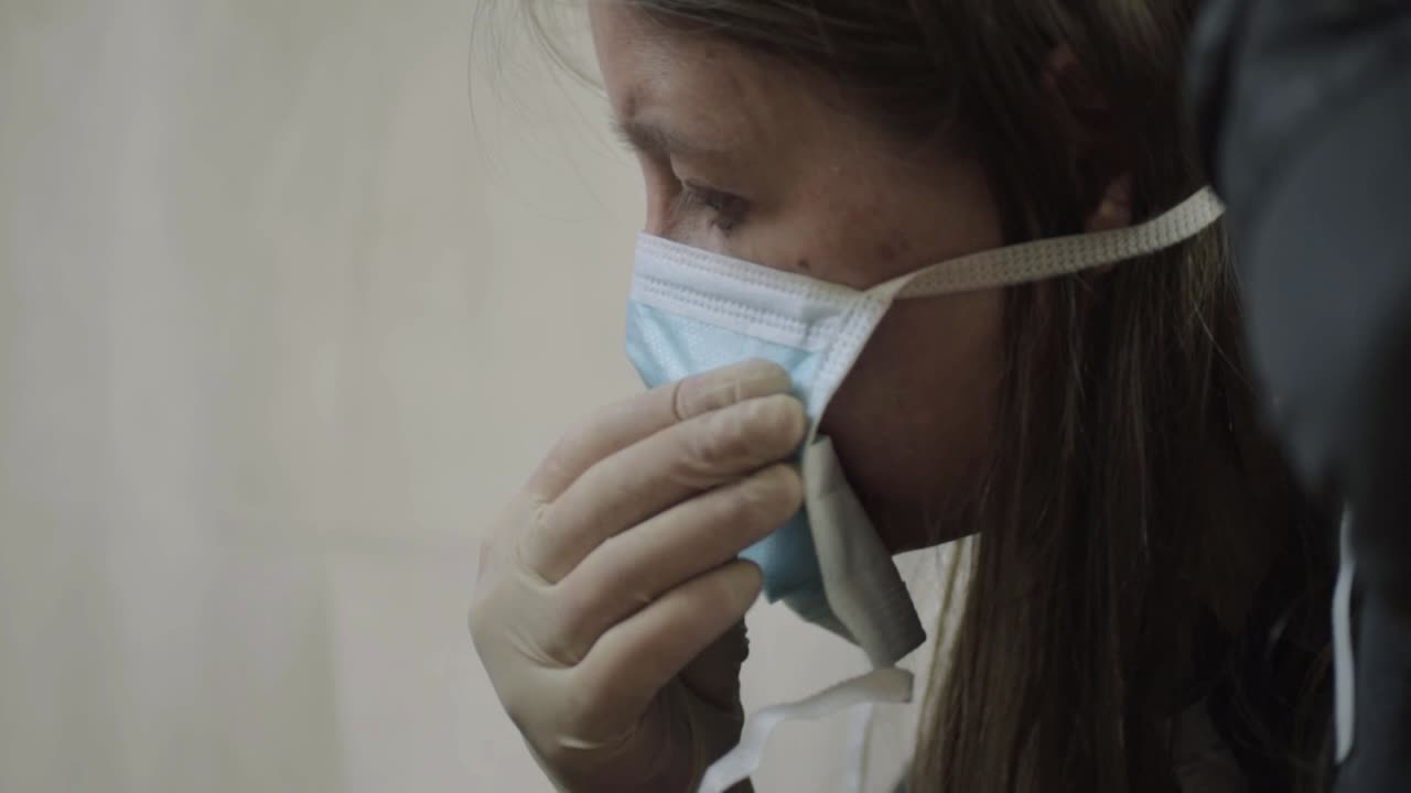 Donna che indossa guanti chirurgici mentre si mette una mascherina chirurgica, inquadratura media del volto
